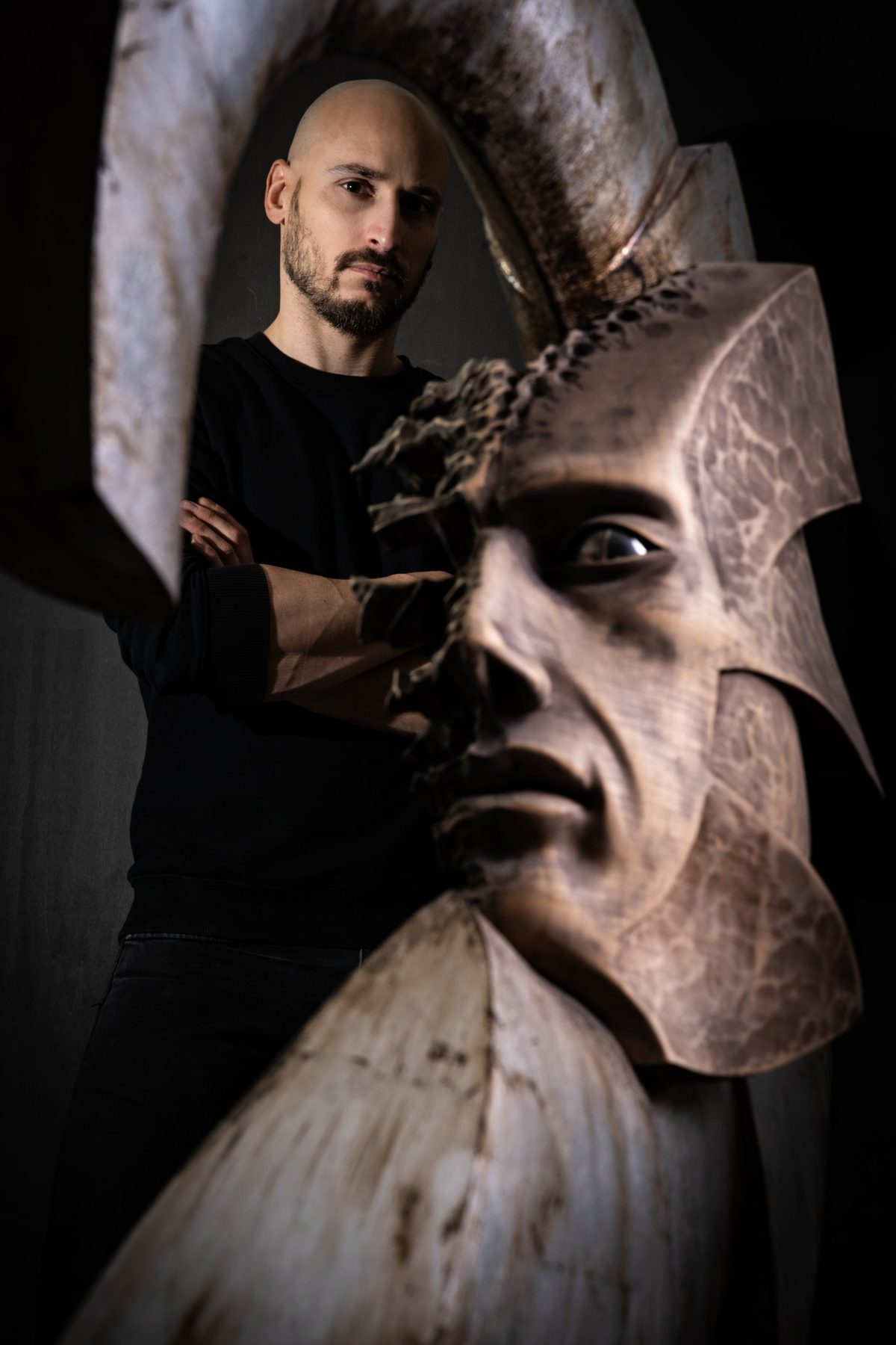 Luca Zuliani, scultore, accanto a una sua scultura in legno raffigurante un volto con elmo